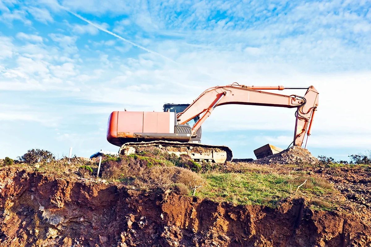 A large orange and black excavator on top of a hill.