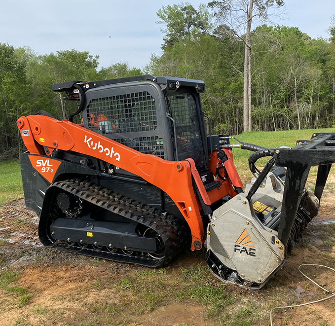 A small orange and black tractor with a large tree in the background.